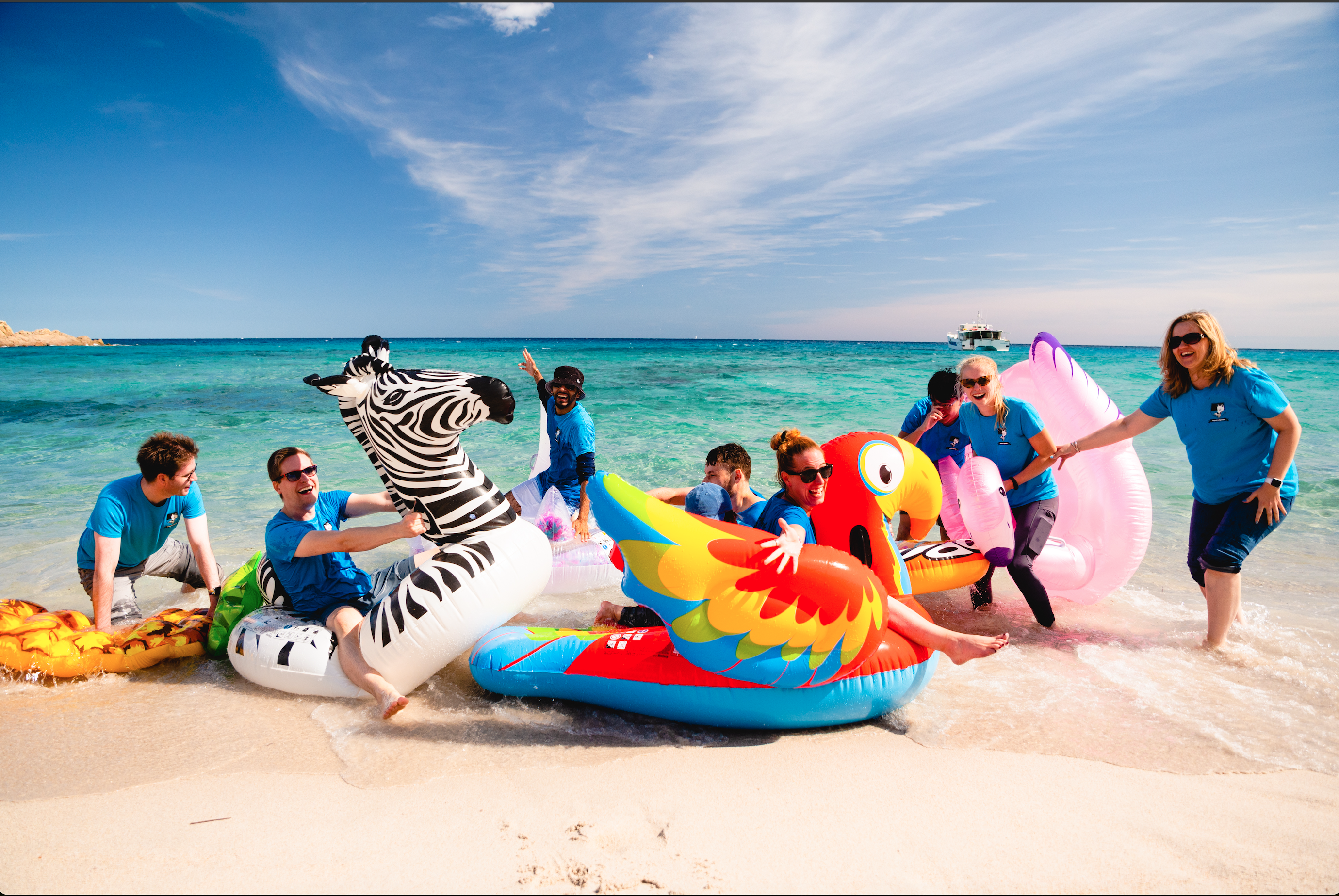 Group on big pool inflatables on the beach with clear blue sea behind
