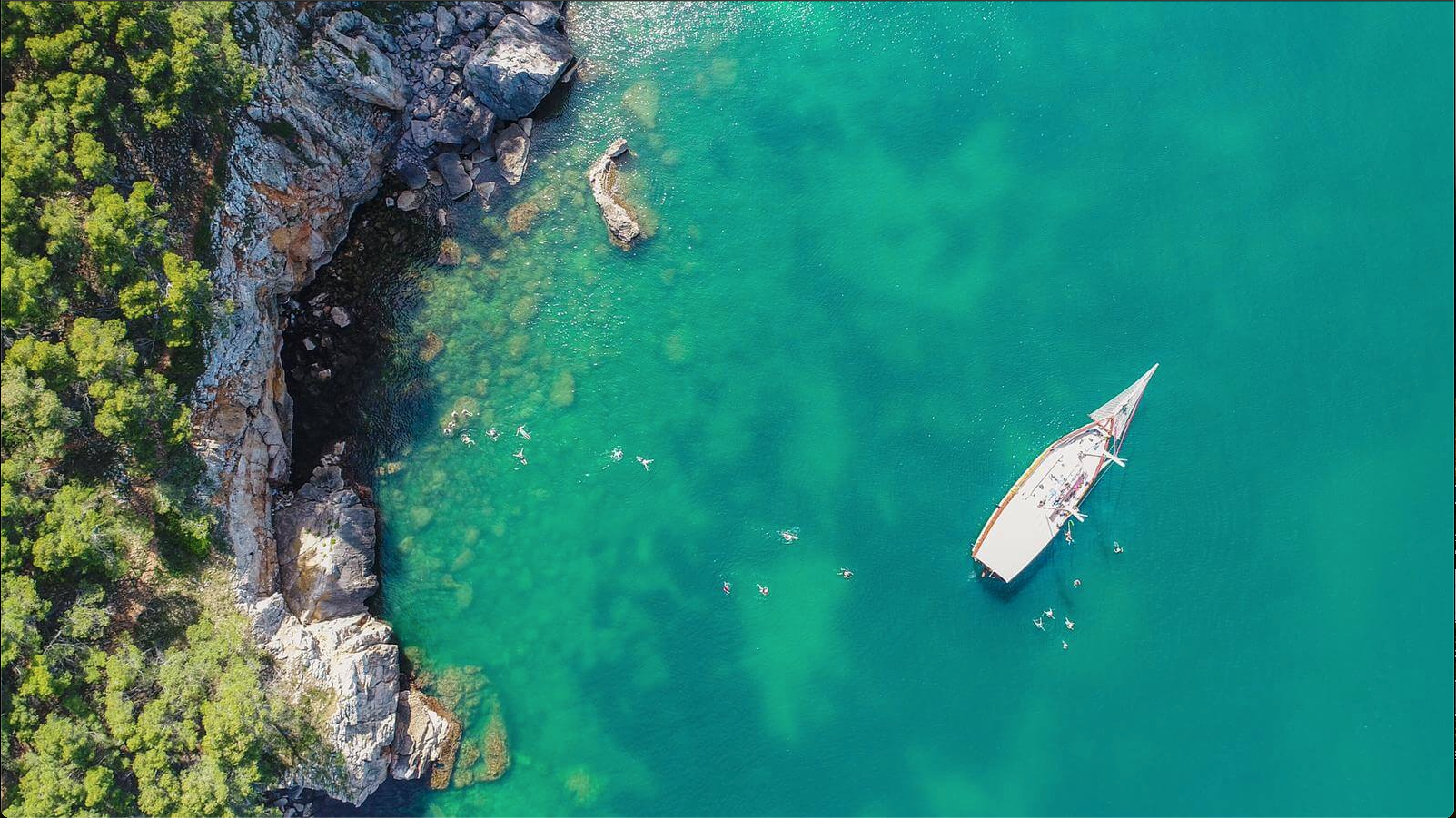 Birdseye view of a large sailing boat with swimmers in turqouise water